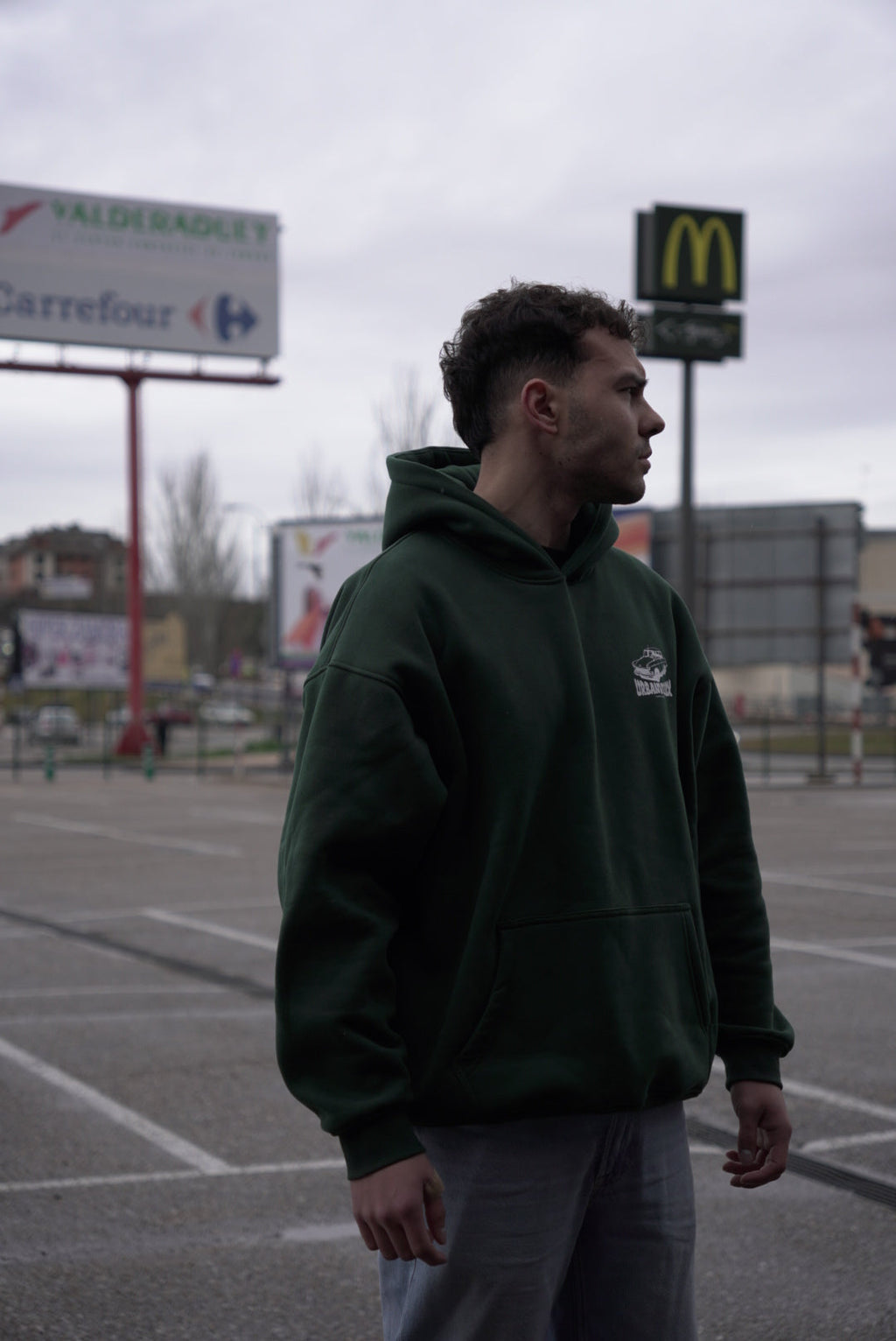 Modelo con Hoodie Urban Essentials verde en exterior urbano - sudadera streetwear oversize UVX Studio