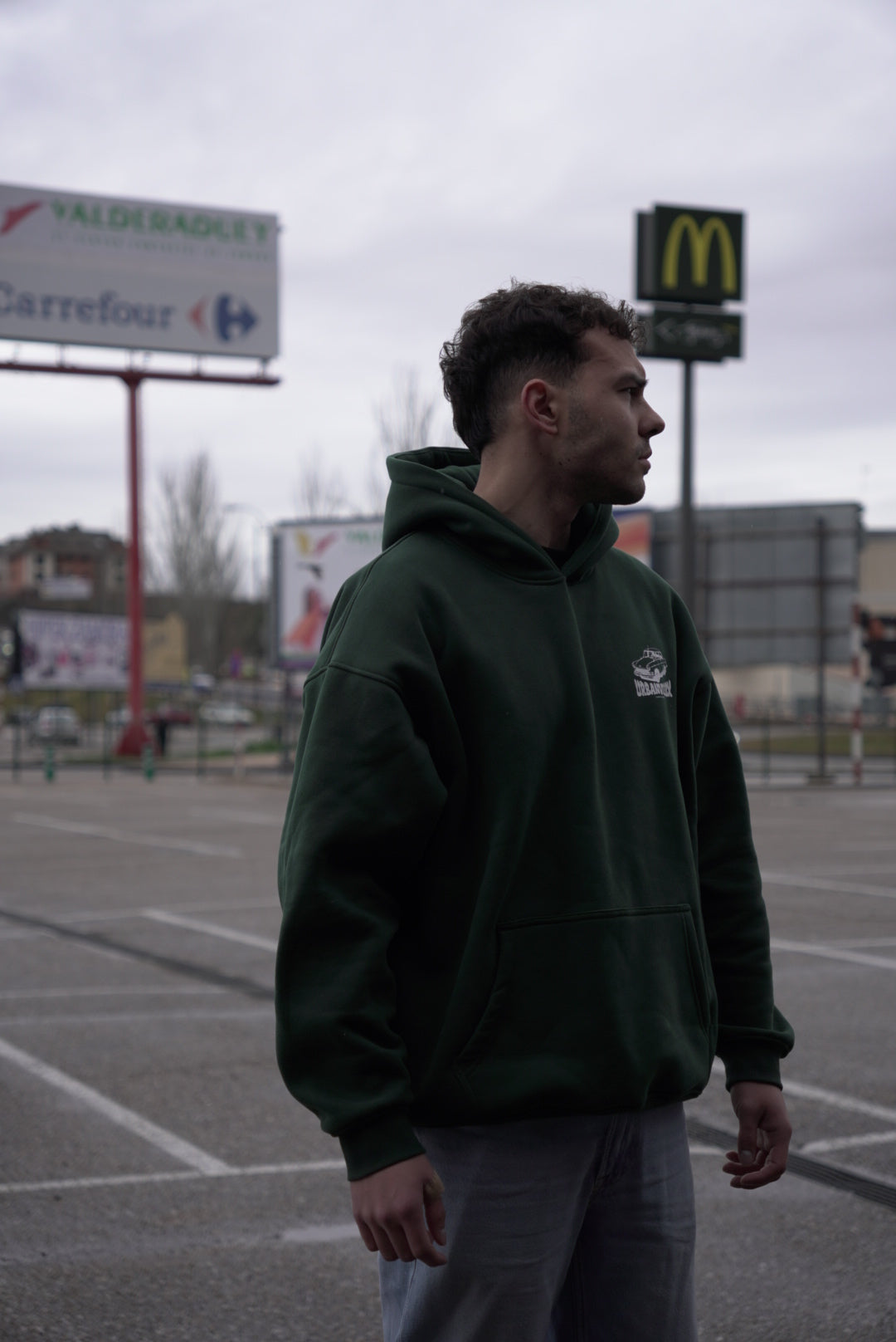 Modelo con Hoodie Urban Essentials verde en exterior urbano - sudadera streetwear oversize UVX Studio